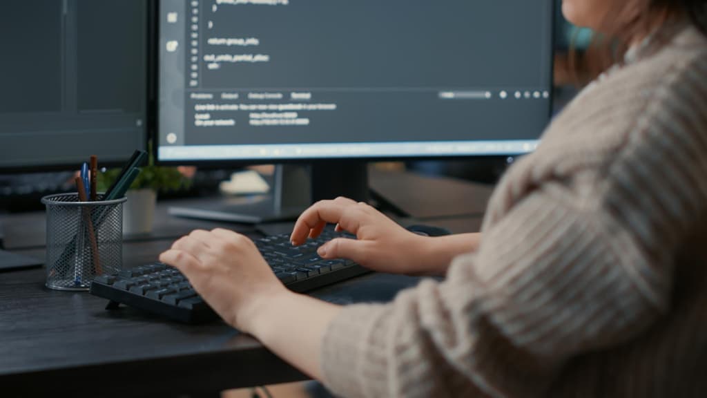 Programmer typing on keyboard in front of computer screens